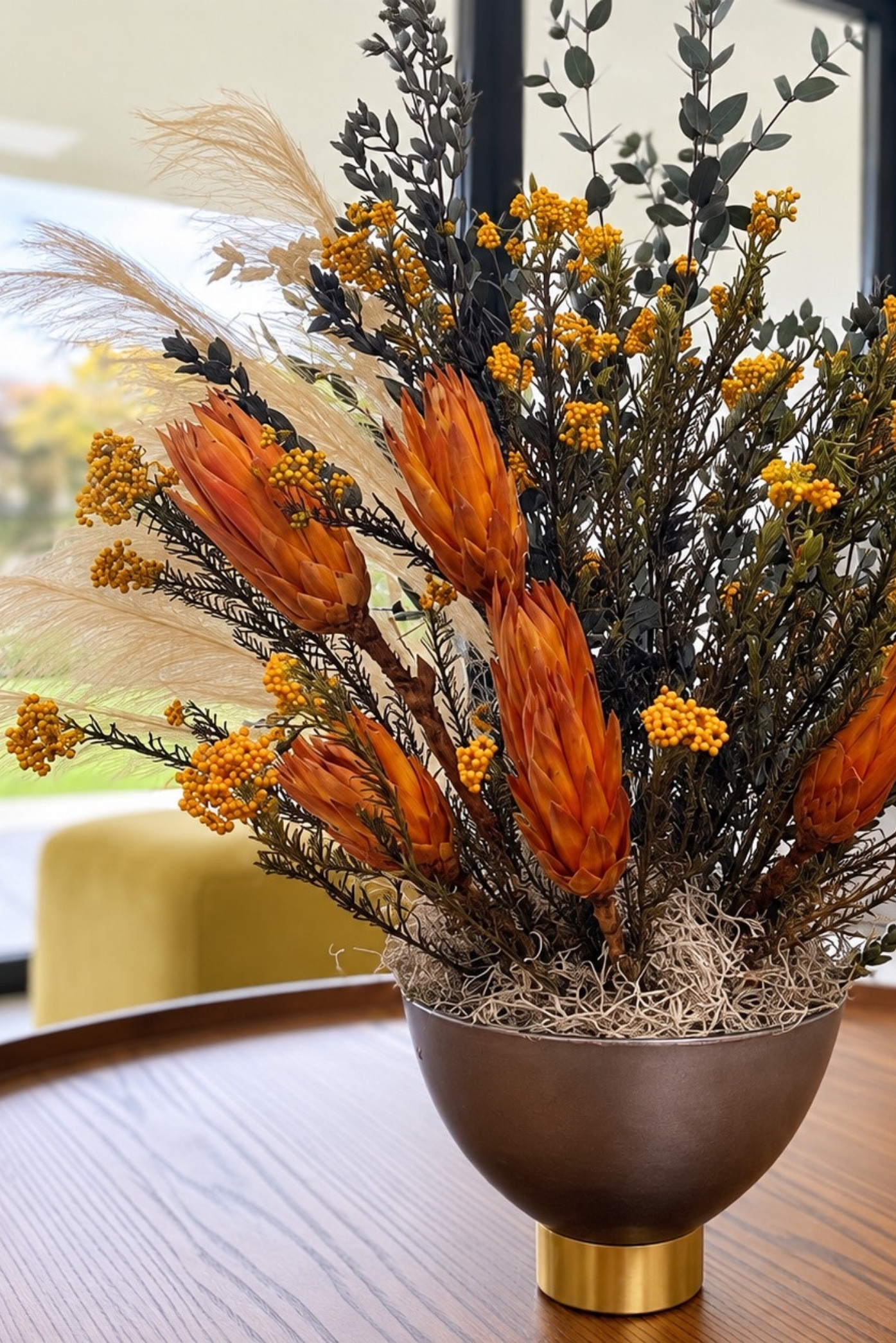Proteas naranjas, flores amarillas, eucalipto y pampas preservados en una copa de bronce