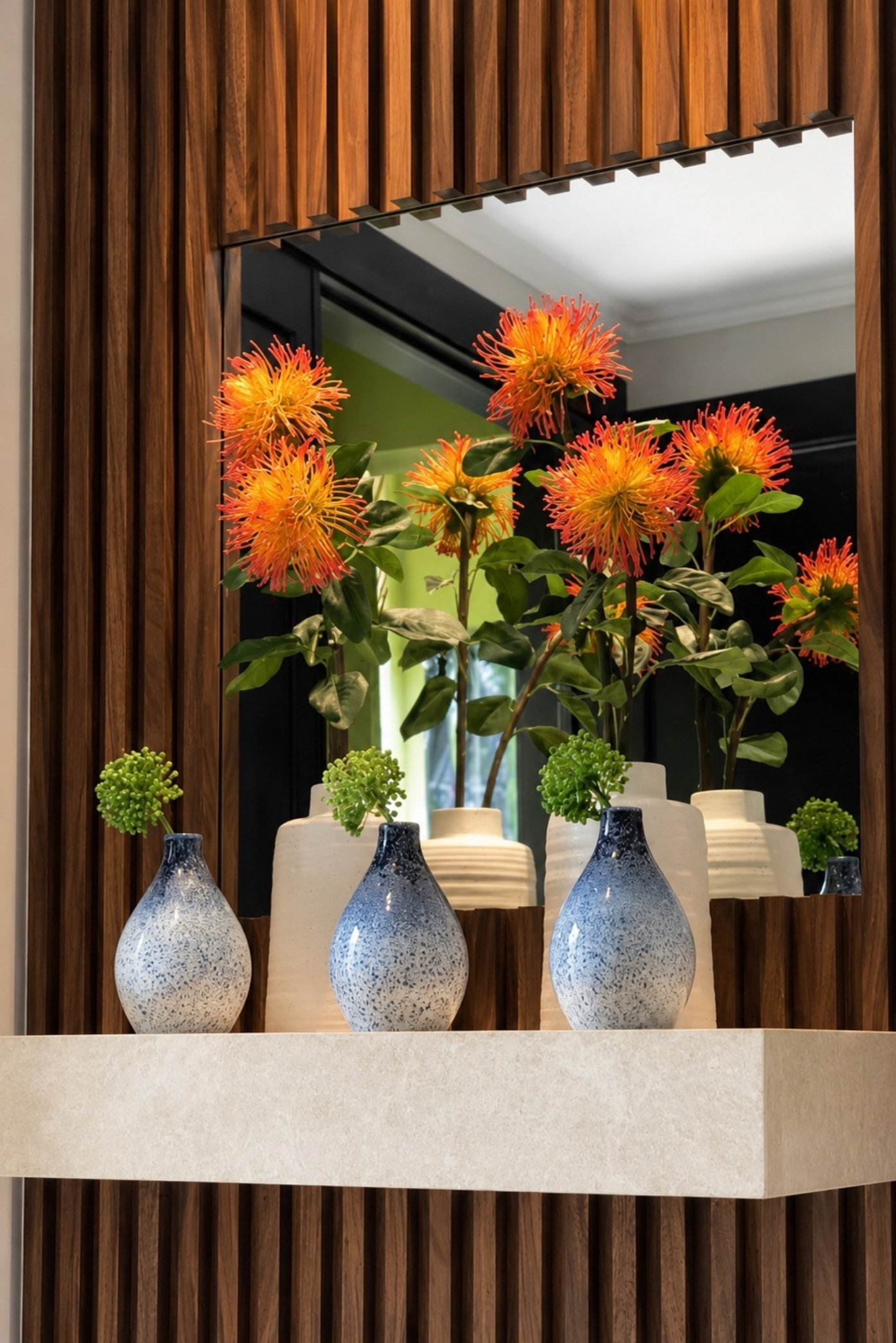 Flores naranjas de protea en jarrones moteados de azul frente a un espejo con marco de madera