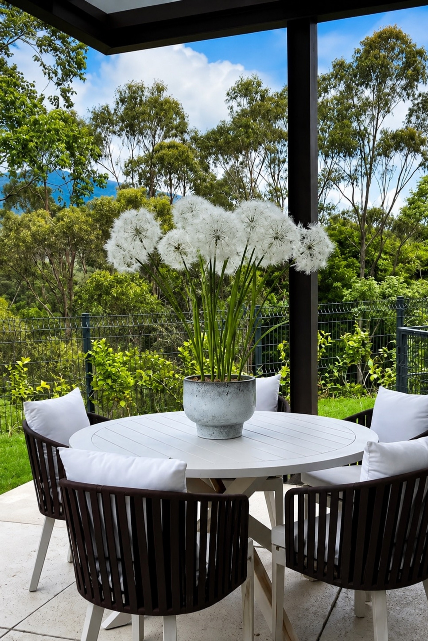 Flores blancas esféricas tipo diente de león en un macetero de piedra sobre una mesa de terraza