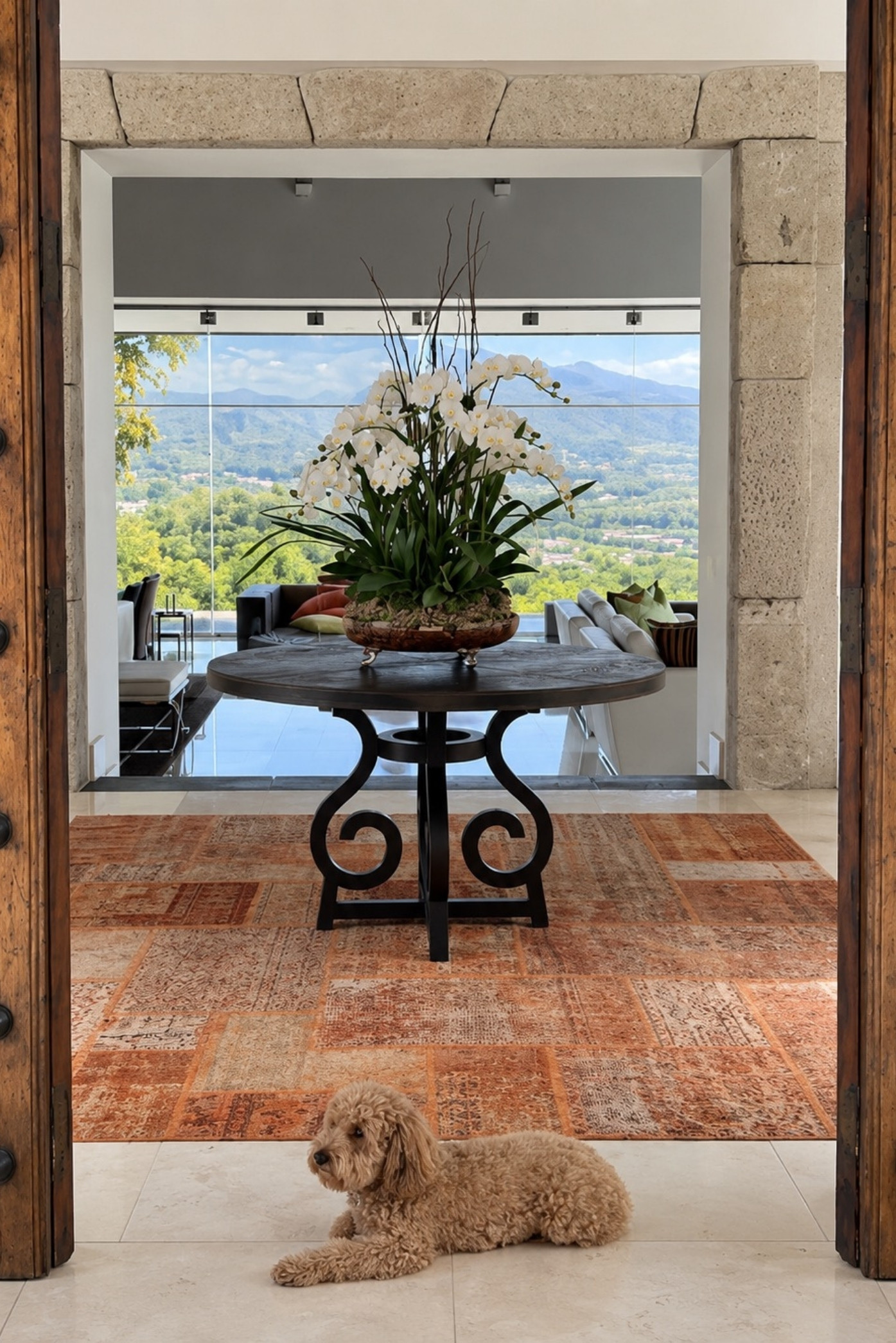 Arreglo alto de orquídeas blancas sobre una mesa redonda de hierro en un vestíbulo con vista al valle