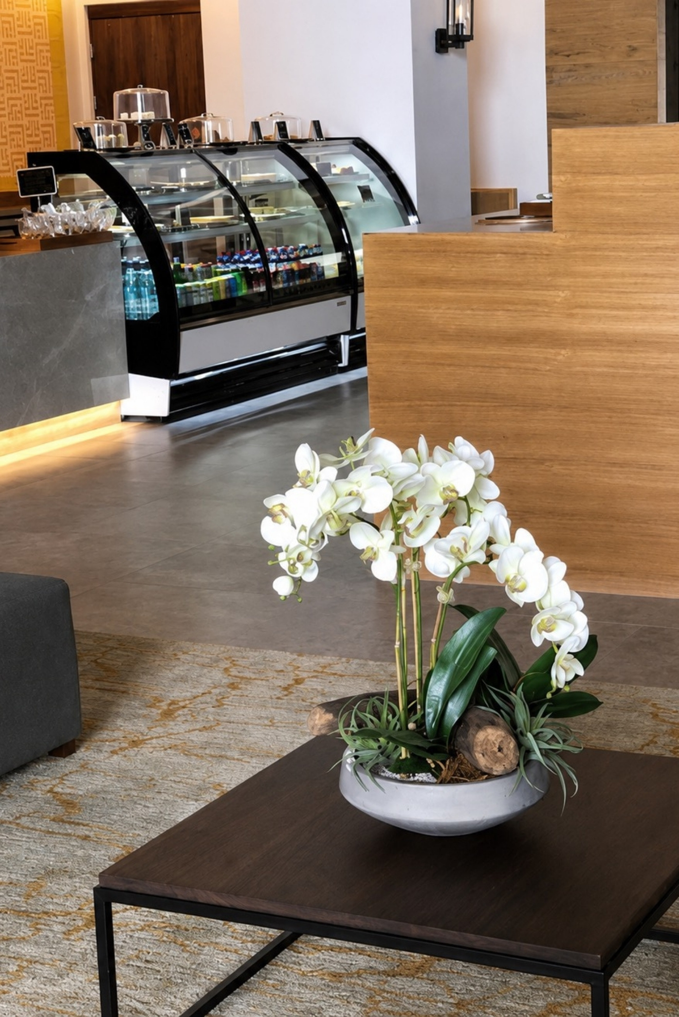 Orquídeas blancas en un cuenco gris sobre una mesa baja, junto a la vitrina de una cafetería