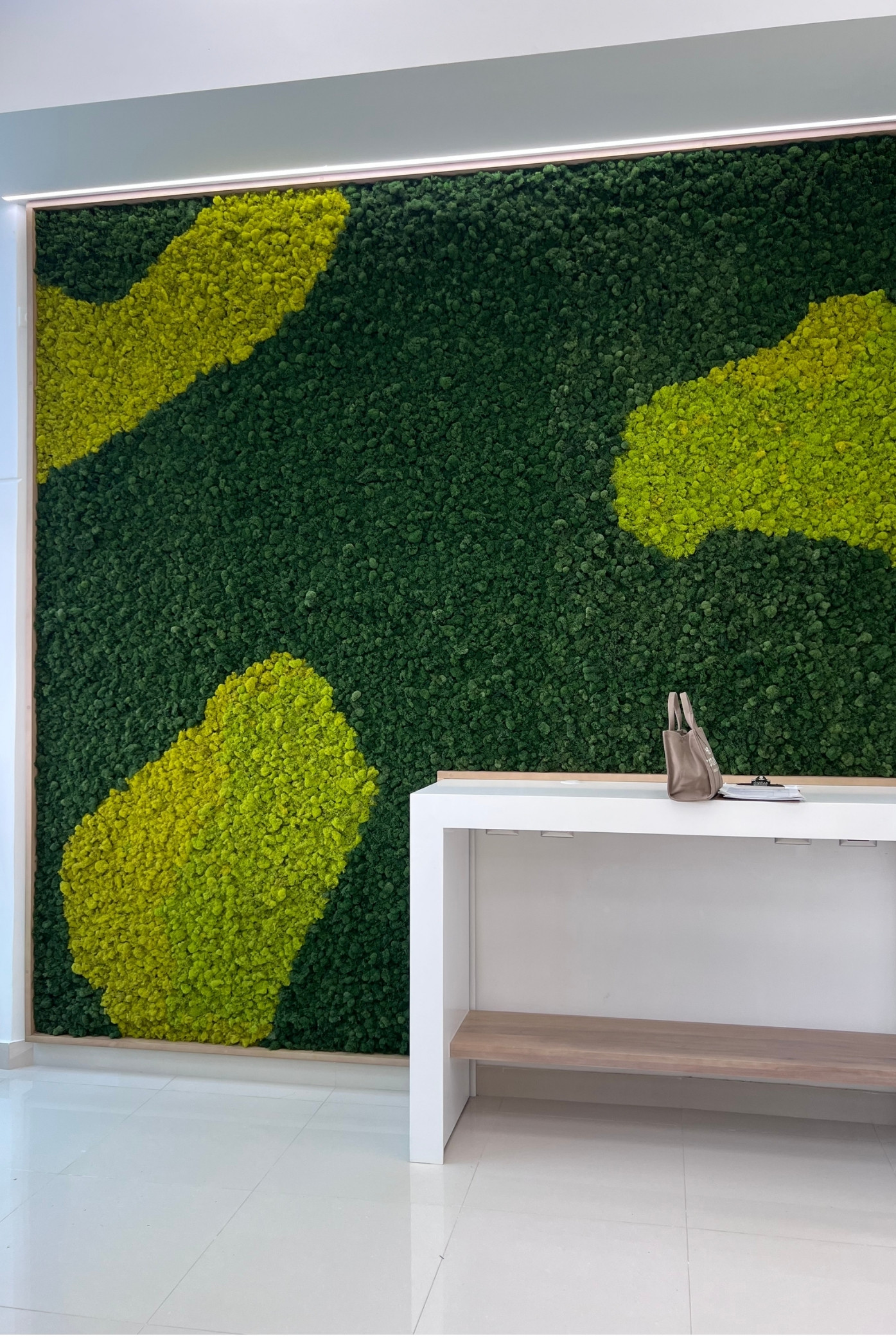 Pared de musgo verde oscuro con formas orgánicas verde lima detrás de una consola blanca
