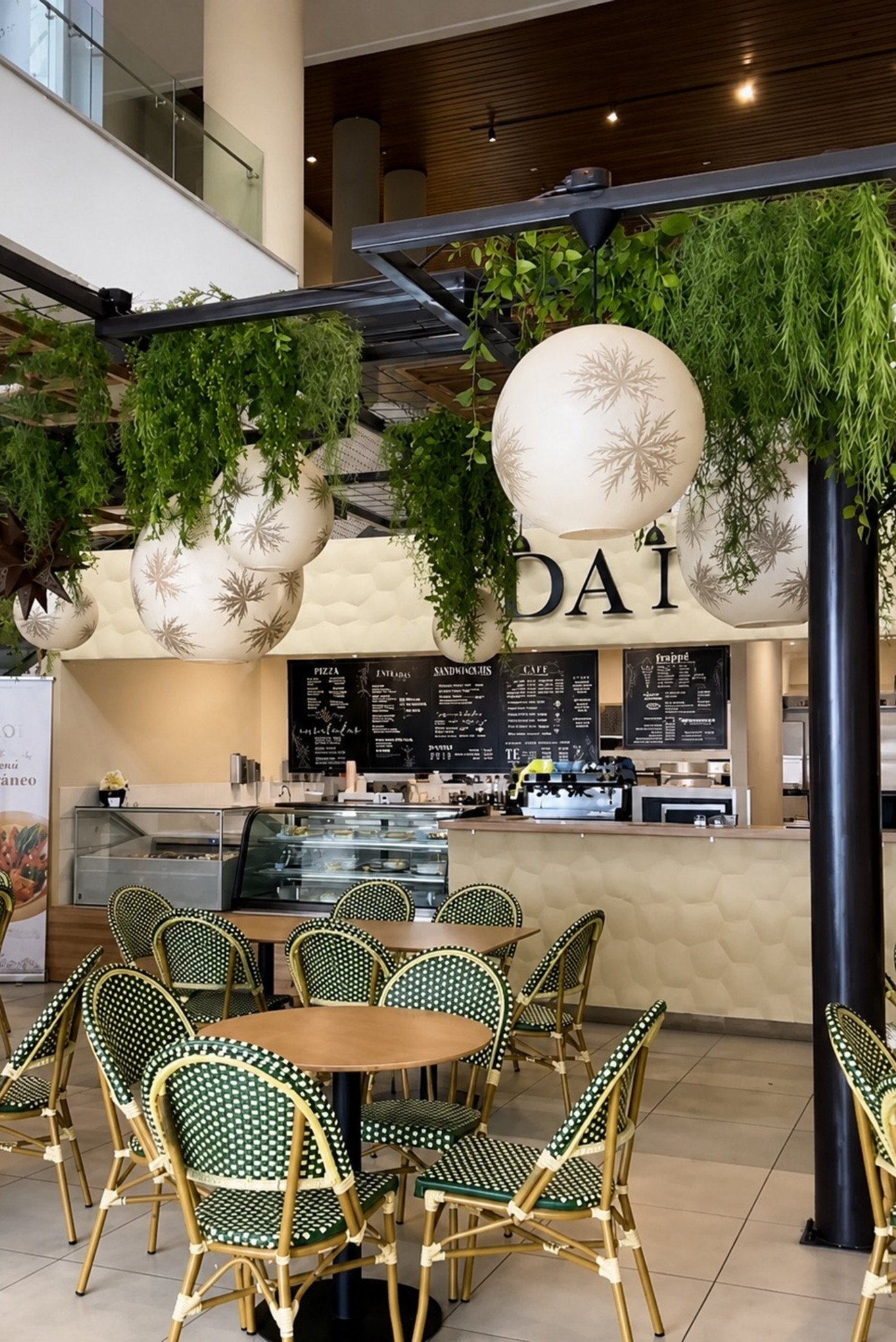 Pérgola metálica con helechos colgantes y lámparas esféricas sobre las mesas de una cafetería