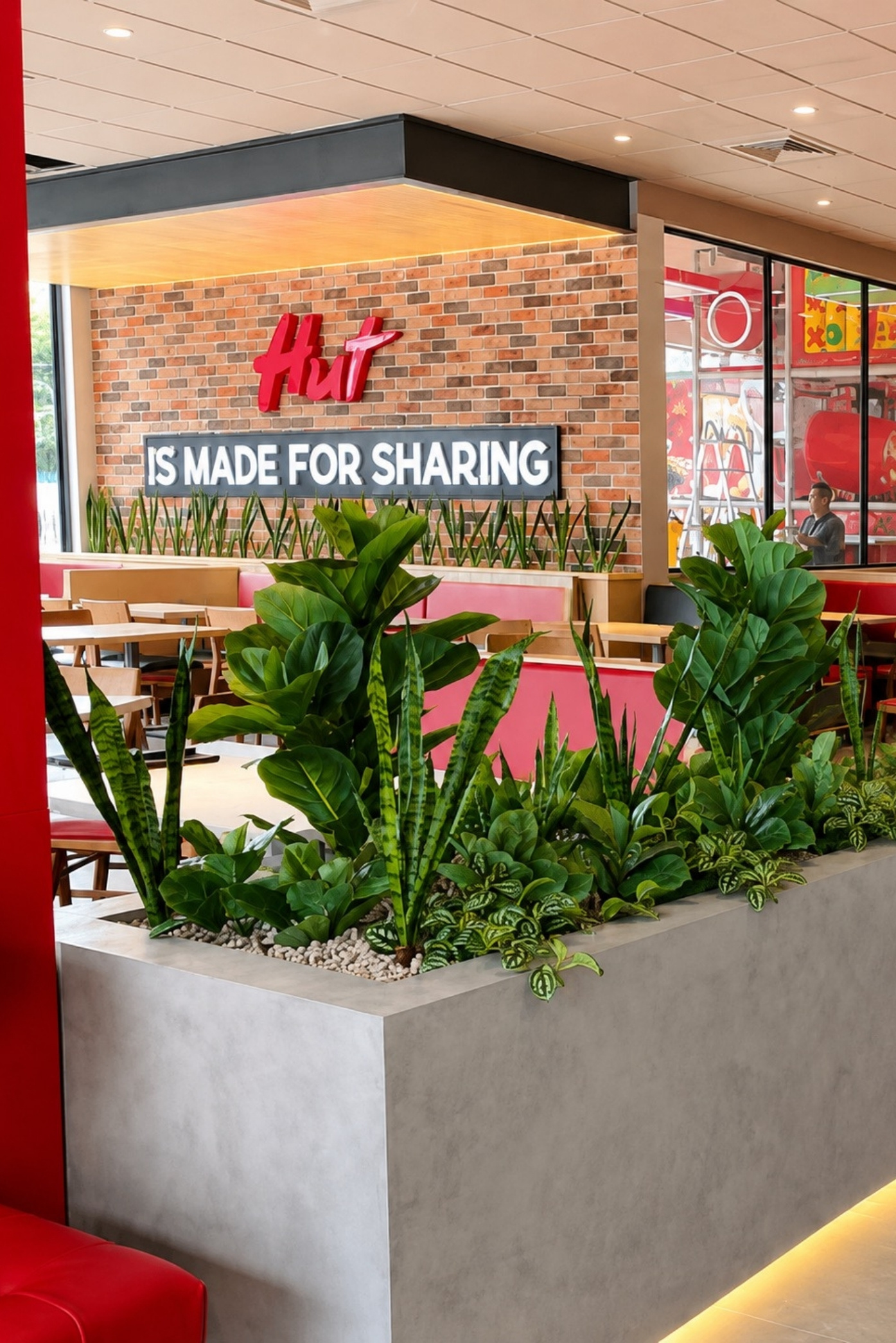 Jardinera de concreto con sansevierias y follajes tropicales junto a las mesas del restaurante