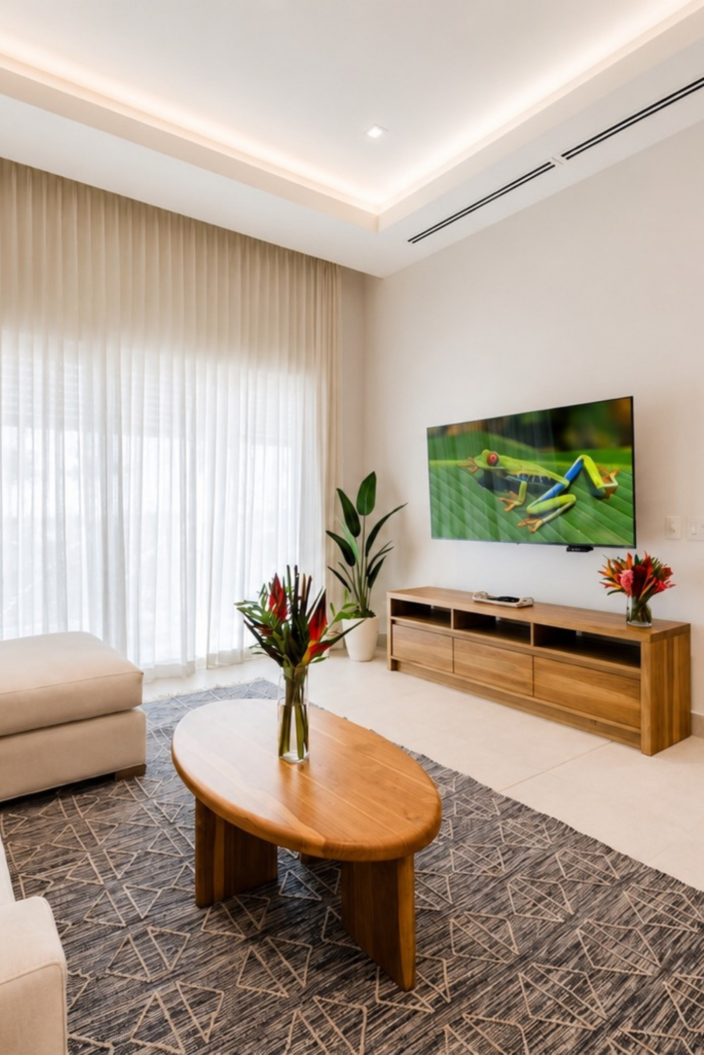 Sala con una planta junto al mueble del televisor y arreglos de heliconias sobre las mesas